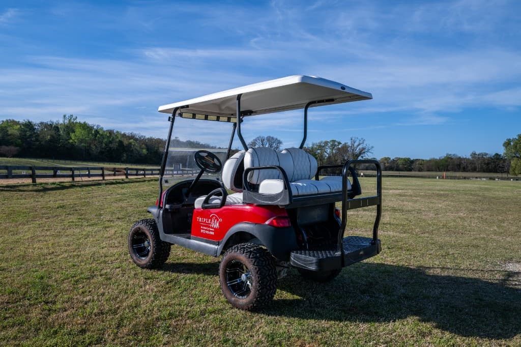 Red Triple W golf cart with rear seats and a white roof, photographed from behind